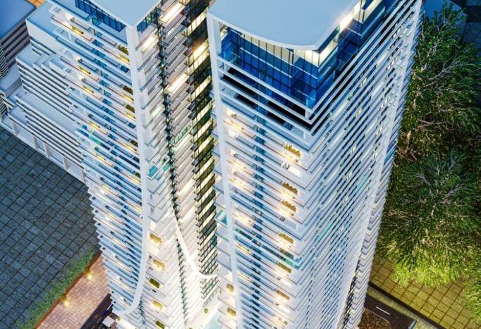 Vue aérienne d'un gratte-ciel moderne de Dubaï la nuit, illuminé et présentant des conceptions architecturales uniques et ondulées avec des voitures garées à la base.