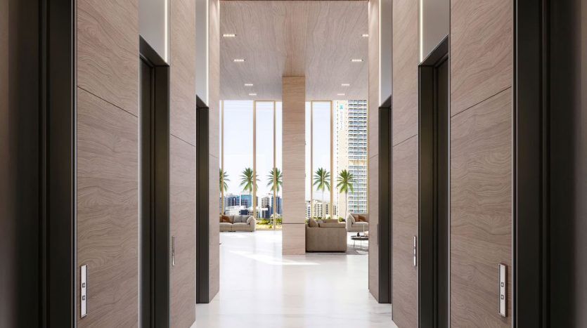 Un hall d'hôtel luxueux à Dubaï avec des sols en marbre, flanqué de plusieurs ascenseurs aux murs en panneaux de bois. Le lobby se prolonge dans un espace bien éclairé avec de grandes fenêtres révélant des palmiers à l'extérieur.