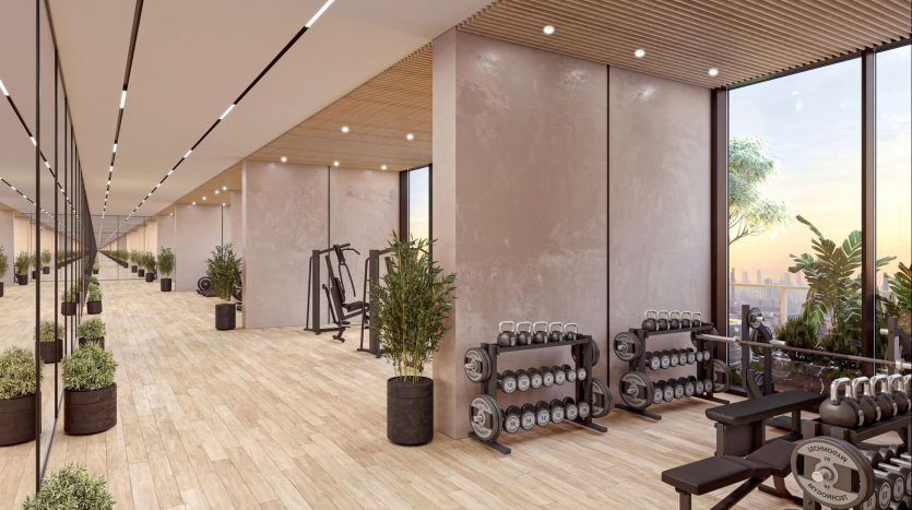 Intérieur de salle de sport moderne comprenant des tapis roulants, des poids libres et de grandes fenêtres offrant une vue sur la ville de Dubaï au coucher du soleil, décoré de plantes d'intérieur et d'un éclairage chaleureux.