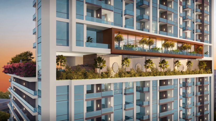 Immeuble d'appartements moderne à Dubaï au crépuscule présentant des balcons en verre et des jardins en terrasse verdoyants contre un ciel coucher de soleil.