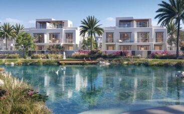Villas résidentielles de luxe à Dubaï surplombant un lac artificiel tranquille aux eaux bleu clair. Des jardins luxuriants et des palmiers entourent la zone, renforçant la sérénité du cadre. Les cygnes nagent paisiblement