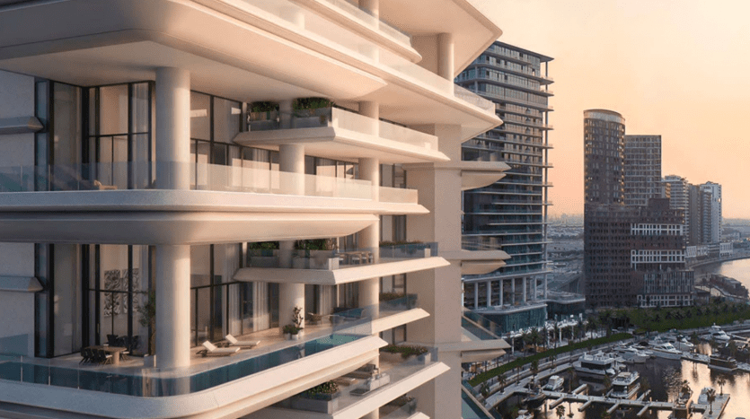 Un complexe d'appartements moderne en bord de rivière à Dubaï, doté de balcons superposés, surplombe un paysage urbain au coucher du soleil, présentant un mélange de styles architecturaux et une marina avec des bateaux.
