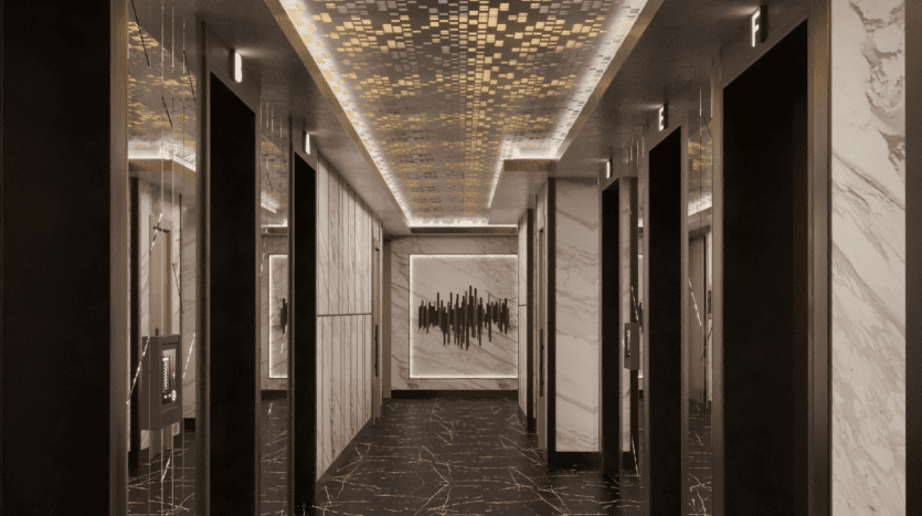 Un couloir d'hôtel moderne présentant des murs en marbre et un sol noir avec des veines dorées. Le plafond présente une mosaïque de carreaux dorés et une grande œuvre d'art abstrait est suspendue au bout du couloir, rappelant