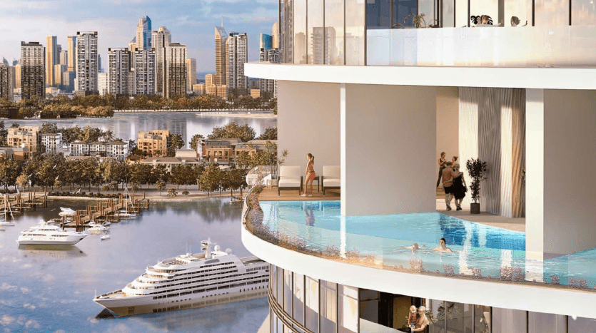 Des balcons d'appartements luxueux de grande hauteur avec une piscine à débordement surplombant un bord de rivière pittoresque et les toits de la ville de Dubaï, avec des bateaux amarrés en contrebas et des gens profitant de l'ambiance ensoleillée.