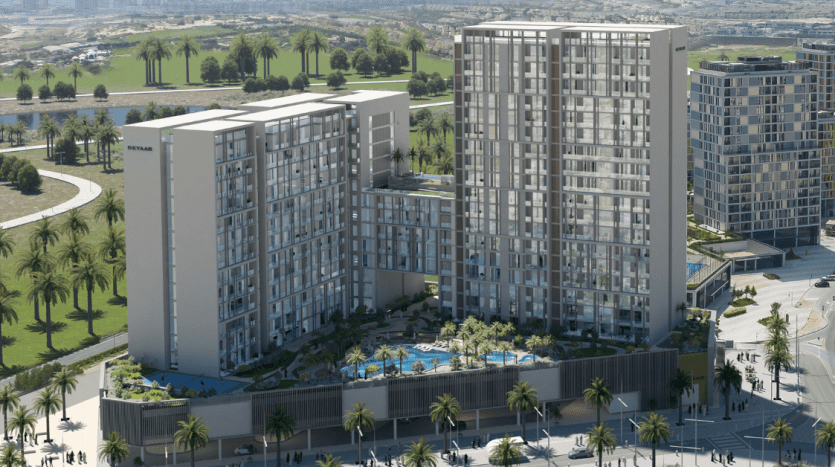 Vue aérienne d'un complexe résidentiel moderne à Dubaï comprenant plusieurs immeubles de grande hauteur aux façades de verre, entourés d'une verdure luxuriante et d'une piscine, situés à proximité d'une zone côtière avec des routes et des parcs visibles