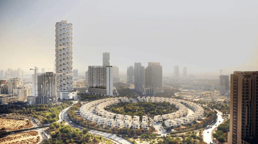 Vue aérienne d'un paysage urbain présentant des structures résidentielles circulaires entourées de routes courbes, avec des immeubles modernes de grande hauteur en arrière-plan sous un ciel brumeux à Dubaï.