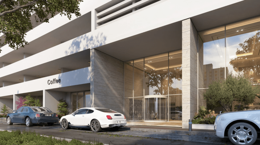 Un café moderne à l'extérieur doté de grandes fenêtres en verre, niché dans un élégant bâtiment de plusieurs étages à Dubaï. Deux voitures sont garées devant, au milieu d’un écrin de verdure et d’un doux soleil.