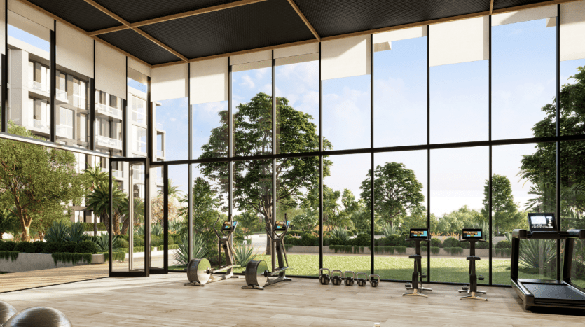 Intérieur de salle de sport moderne dans une villa de Dubaï avec de vastes murs de verre offrant une vue panoramique sur la verdure luxuriante à l'extérieur. L'espace comprend des vélos d'exercice, des poids et un tapis roulant, mélangeant harmonieusement les éléments intérieurs et extérieurs.