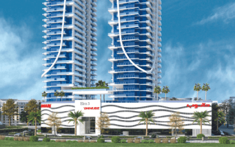 Un immeuble résidentiel moderne de grande hauteur avec des balcons blancs incurvés compensés par du verre bleu sous un ciel clair, entouré d'un aménagement paysager vert et doté d'une *agence immobilière Dubaï* à la base