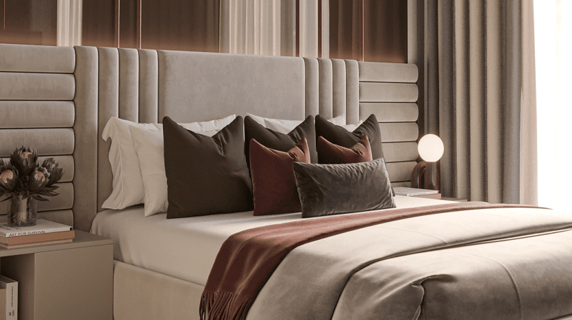 Une chambre luxueuse dans une villa de Dubaï comprenant un grand lit avec une tête de lit haute et rembourrée, recouverte d'oreillers blancs, beiges et rouge foncé. Une table de chevet contient une lampe et un vase avec
