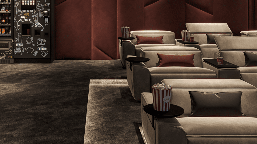 Salle de cinéma de luxe dans un appartement de Dubaï comprenant des rangées de fauteuils inclinables gris moelleux avec des coussins roses, des tables d'appoint avec du pop-corn et un snack-bar faiblement éclairé en arrière-plan.
