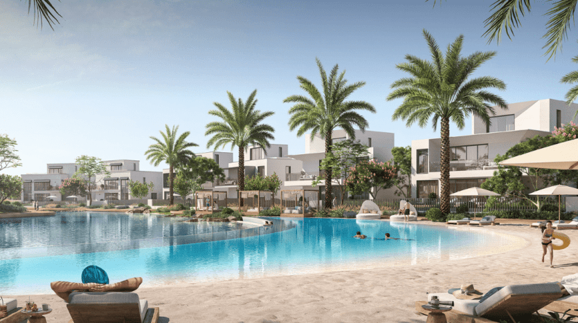 Un complexe luxueux avec des bâtiments blancs modernes entourés de palmiers au bord d'une grande piscine incurvée avec des bordures de sable. Les gens se détendent sur des chaises longues et nagent près d’une superbe villa à Dubaï.