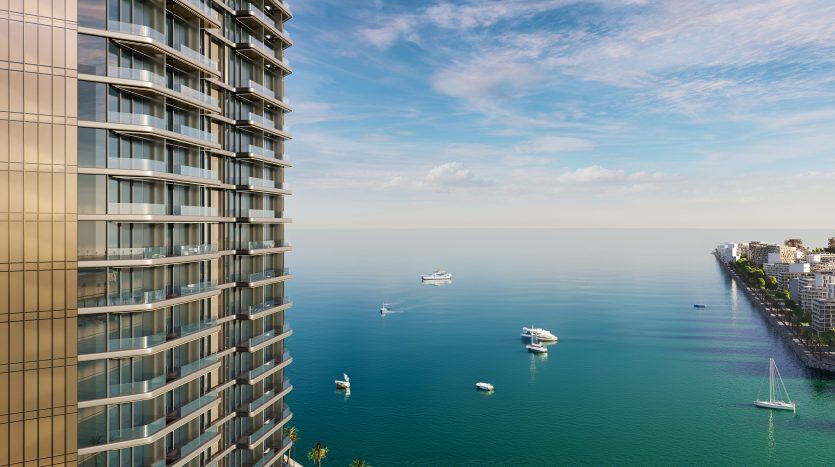 Vue panoramique depuis un immeuble de grande hauteur surplombant l'océan à Dubaï, avec plusieurs bateaux sur l'eau et un horizon de ville côtière sur la droite.