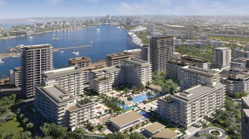 Aerial view of a modern seaside residential district with several high-rise buildings, lush green spaces and a bustling marina with boats, all overlooking the city's rooftops and the Dubai River.