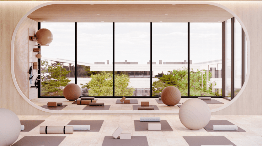 Studio de yoga moderne doté d'une grande fenêtre ovale donnant sur une cour, remplie de ballons d'exercice, de tapis et de blocs sur un parquet en bois. Une lumière vive et naturelle améliore l'ambiance sereine, idéale pour les immobiliers recherchant