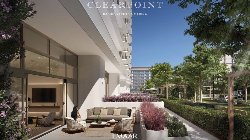 A luxurious balcony with soft seating overlooks a landscaped garden and marina, part of the Clearpoint residential complex in Dubai, highlighted by skyscrapers and lush greenery.