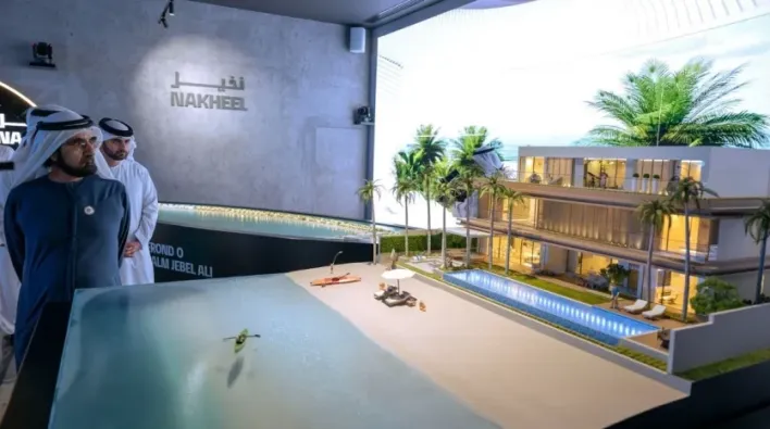 Deux hommes examinent un modèle architectural détaillé d'un immeuble résidentiel moderne et du paysage environnant à Dubaï, exposé sous un éclairage intense dans une pièce avec la marque de l'entreprise sur le mur du fond.