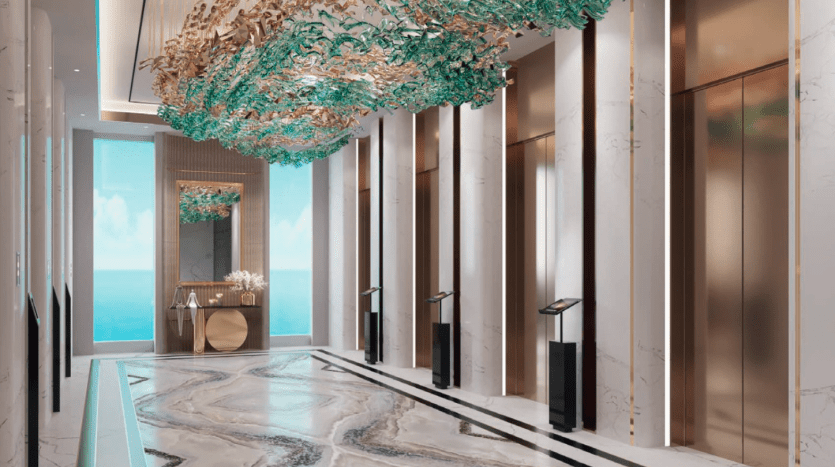 Hall d'entrée luxueux avec sols en marbre, accents dorés et sculpture décorative au plafond en verre. Des plantes élégamment placées et des vues scintillantes sur l'océan sont visibles depuis les grandes fenêtres, parfaites pour ceux intéressés par un investissement.