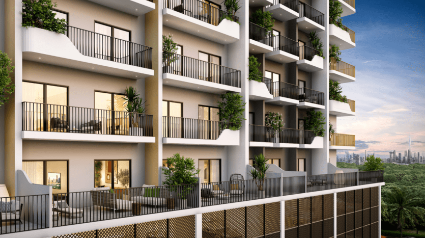 Un immeuble d'appartements moderne de plusieurs étages à Dubaï, doté de balcons avec balustrades et plantes, au crépuscule, avec une ligne d'horizon de la ville au loin.