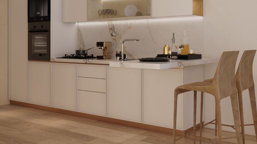 Une cuisine moderne avec armoires beiges, dosseret en marbre et appareils électroménagers intégrés. Deux tabourets de bar se trouvent devant un comptoir avec des ustensiles de cuisine et des plantes dans une luxueuse villa de Dubaï.