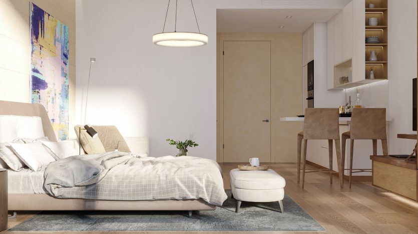Chambre moderne dans un appartement de Dubaï avec un lit soigneusement fait, un petit pouf, des œuvres d'art murales abstraites et une suspension. Cette chambre offre une vue sur un coin cuisine attenant doté de tabourets de bar. Un éclairage naturel doux améliore