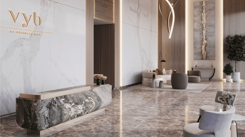 Un hall d'entrée élégant avec un sol et des murs en marbre, avec un élégant comptoir de réception affichant le logo « vyb » en lettres dorées. Un mobilier moderne et une décoration de bon goût rehaussent l'ambiance luxueuse, rappelant
