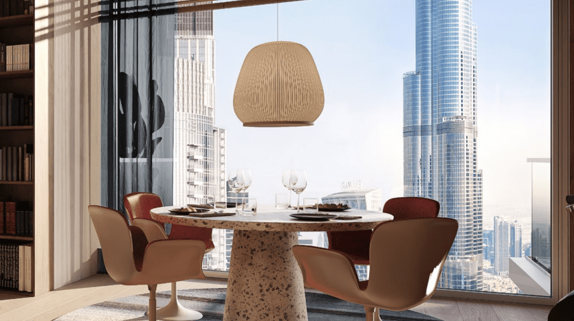 Salle à manger moderne dans un appartement de Dubaï avec une table ronde pour deux, des chaises rouges élégantes, une grande suspension au-dessus, entourée d'étagères, donnant sur un paysage urbain du sol au plafond