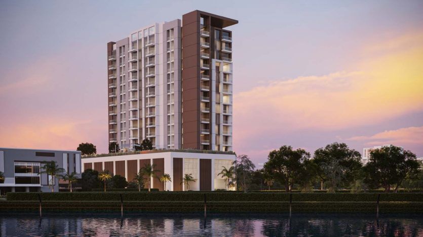 Un immeuble résidentiel moderne de grande hauteur au coucher du soleil, avec un ciel vibrant et des reflets dans un front de mer calme, entouré d'une verdure luxuriante, illustre le premier immobilier de Dubaï.