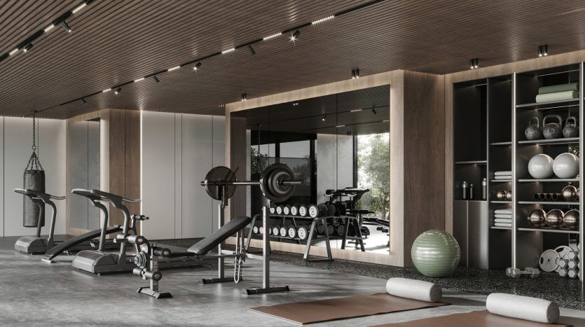 Salle de sport moderne à domicile avec divers équipements d'exercice, notamment des tapis roulants, des poids et un vélo, avec des touches de bois et de grandes fenêtres en verre dans un appartement de Dubaï.