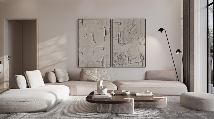 Salon moderne dans une propriété de l'immobilier Dubaï, doté de canapés minimalistes beiges, d'une table basse en bois avec des objets décoratifs et d'œuvres d'art abstraites au mur, éclairé par la lumière naturelle provenant de grandes fenêtres.