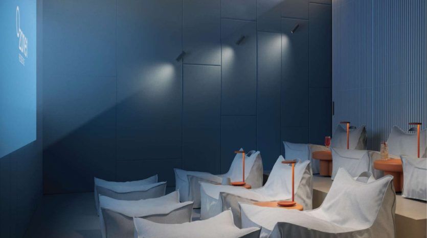 Une salle à manger moderne et minimaliste dans une villa de Dubaï avec des chaises blanches recouvertes de draps de protection transparents et des mégaphones orange sur les tables, dans une pièce faiblement éclairée aux murs bleus et à l'éclairage subtil.