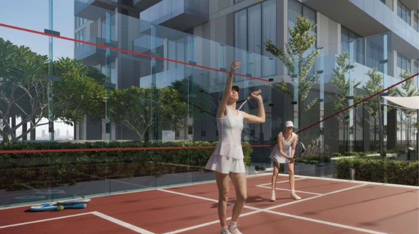 Deux femmes jouant au badminton sur un terrain extérieur entouré de bâtiments modernes et de verdure dans une villa du quartier de Dubaï, avec une femme servant le volant sous un ciel clair.