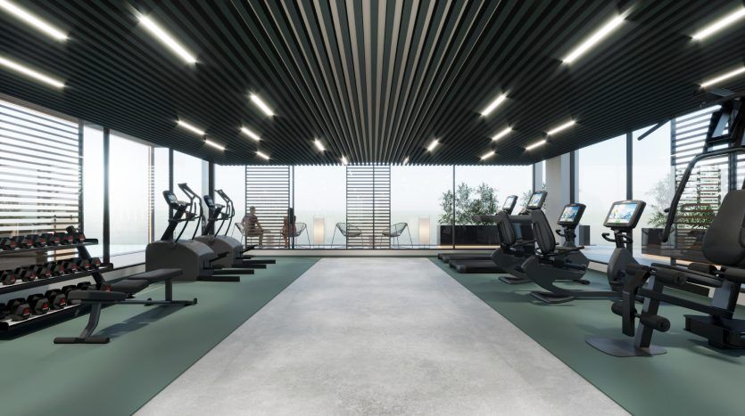 Une salle de sport moderne avec machines cardio et poids donnant sur une baie vitrée, sous un plafond aux lumières linéaires. L'espace est propre, lumineux et bien équipé pour les entraînements, parfait pour les investisseurs axés sur l'immobilier