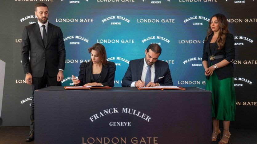 Quatre personnes lors d'un événement de signature pour un investissement Dubaï, avec deux individus assis et signant des documents et deux debout à côté d'eux, devant une bannière avec les logos de l'entreprise.