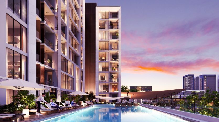 Un immeuble d'appartements luxueux à Dubaï avec une piscine extérieure où les gens se détendent sur des chaises longues au bord de la piscine au coucher du soleil, présentant une architecture moderne avec des balcons et de grandes fenêtres.