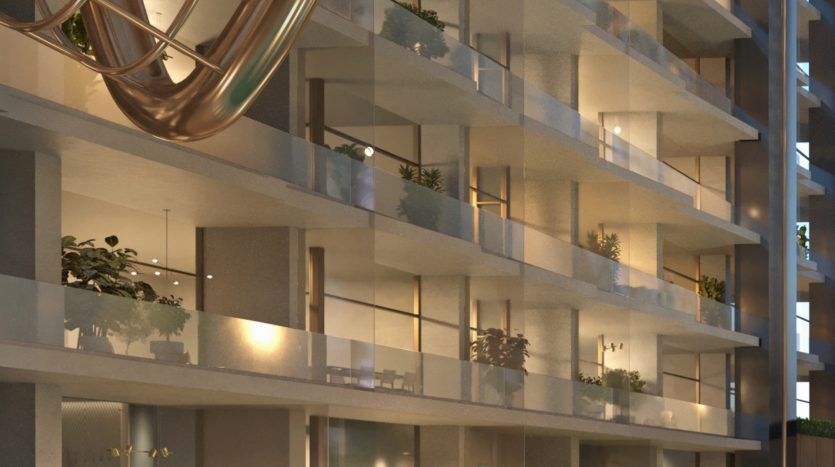 Immeuble résidentiel moderne de grande hauteur à Dubaï au crépuscule, doté de lumières intérieures lumineuses et de balcons ornés de plantes, avec une sculpture métallique unique traversant la façade.