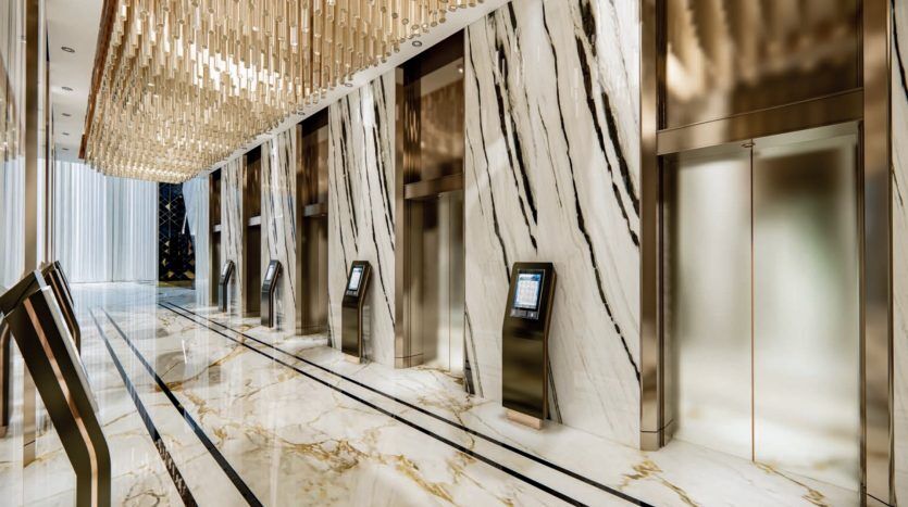 Luxurious lobby of a Dubai hotel featuring a row of elevator doors set into marble walls, a striking golden chandelier and an elegantly designed floor, generating an opulent atmosphere.