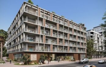 Un immeuble d'appartements moderne à Dubaï avec plusieurs balcons, de grandes fenêtres et des espaces commerciaux au rez-de-chaussée, entouré d'une verdure luxuriante et de rues fréquentées par des voitures et des piétons.