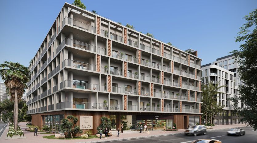 Un immeuble d'appartements moderne à Dubaï avec plusieurs balcons, de grandes fenêtres et des espaces commerciaux au rez-de-chaussée, entouré d'une verdure luxuriante et de rues fréquentées par des voitures et des piétons.