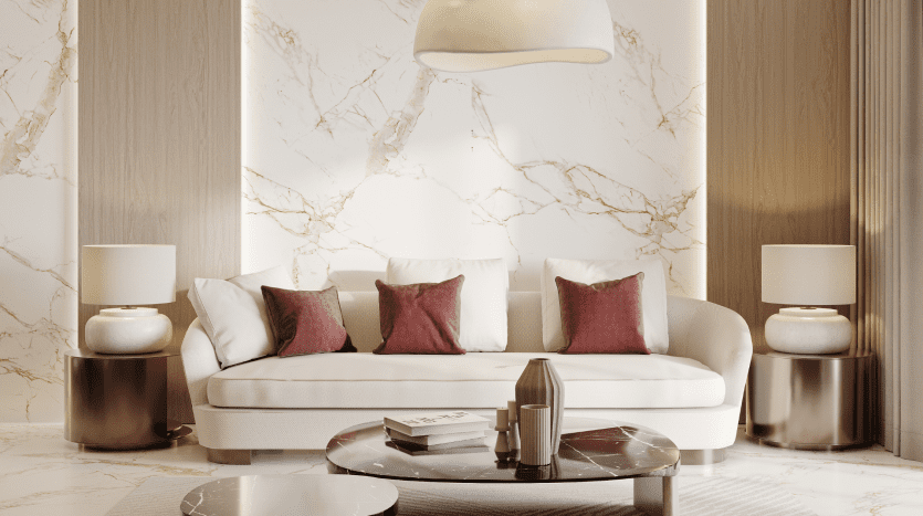 Salon élégant dans un appartement de Dubaï comprenant un canapé blanc avec des oreillers marron, des murs en marbre, une table basse ronde, des livres et des lampes placées symétriquement sur les tables d'appoint.