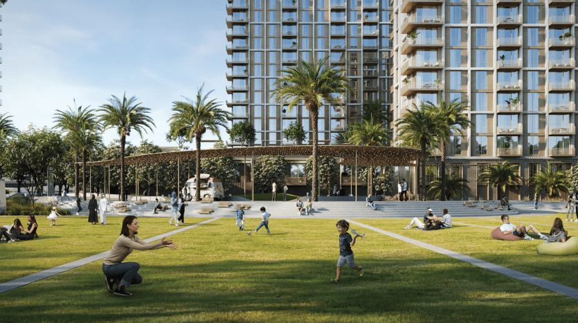 Une scène de parc urbain animée à Dubaï avec des gens profitant d'une journée ensoleillée. De grands bâtiments modernes entourent la zone, avec une herbe luxuriante, des palmiers et un pavillon ombragé. Un enfant court vers un adulte accroupi, les bras ouverts.