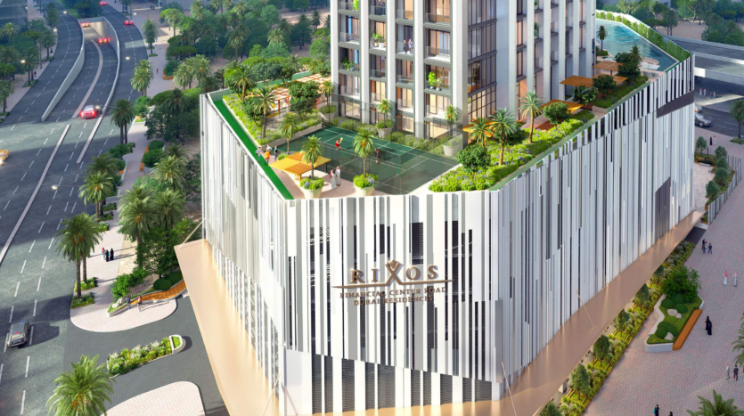 Vue aérienne d'un immeuble moderne de grande hauteur doté d'un toit vert avec des jardins et un court de tennis, entouré de rues urbaines animées et de verdure luxuriante, parfait pour une annonce d'agence immobilière à Dubaï.