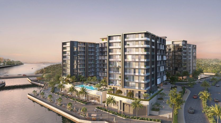 Immeubles d'appartements modernes à Dubaï avec façades de verre au bord d'une rivière au coucher du soleil, avec palmiers, piscine et promenade au bord de l'eau.