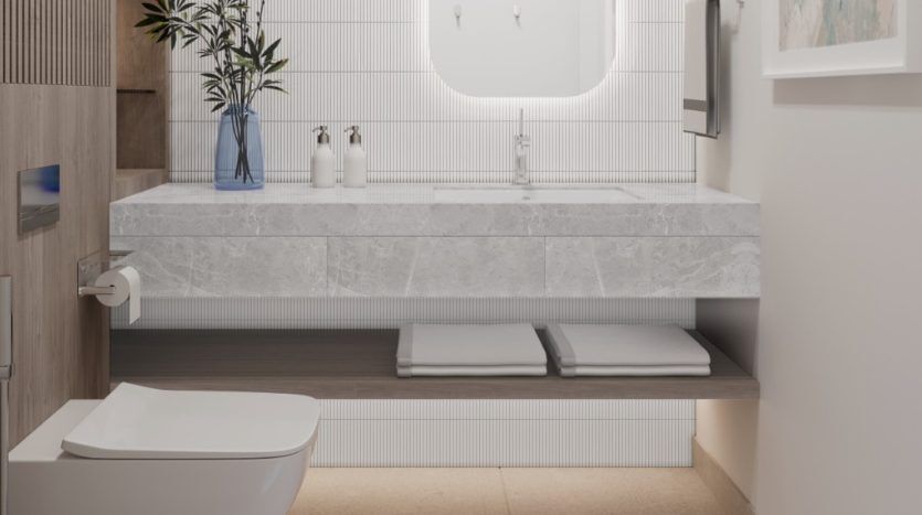 Intérieur de salle de bains moderne dans un appartement de Dubaï comprenant une vanité élégante avec un grand miroir, un comptoir blanc, des armoires en bois et une plante en pot à côté de toilettes minimalistes.
