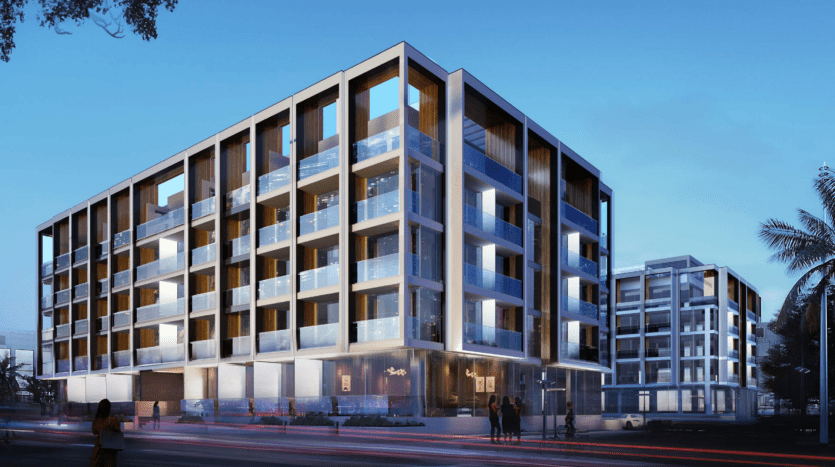 Bâtiment architectural moderne éclairé au crépuscule, doté de grandes fenêtres en verre et d'un design élégant et structuré avec des piétons près de l'entrée, parfait pour être présenté sur le marché immobilier de Dubaï.