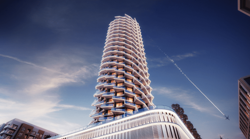 Un grand bâtiment moderne avec des balcons ondulés et de grandes fenêtres en verre sous un ciel bleu clair avec une traînée de jets, situé dans un environnement urbain à Dubaï.