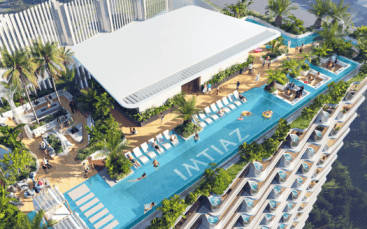Vista aerea di una lussuosa piscina sul tetto di un grattacielo a Dubai, circondata da piante tropicali, con persone che prendono il sole e nuotano.