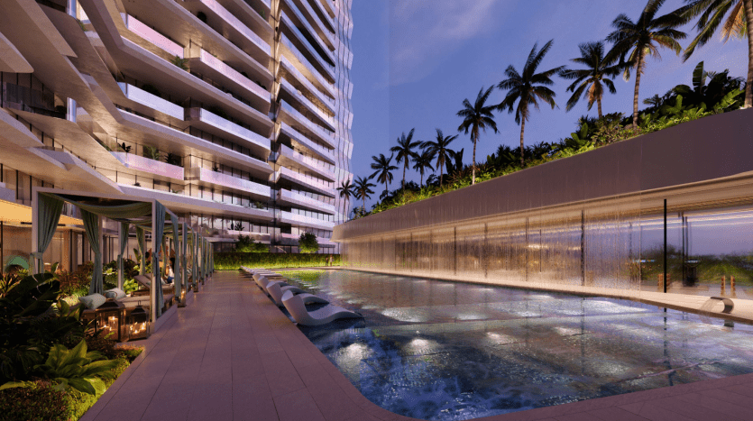 Espace piscine luxueux d'un hôtel à Dubaï au crépuscule, doté d'eau éclairée avec des chaises longues, entouré de palmiers et d'un immeuble moderne de grande hauteur.