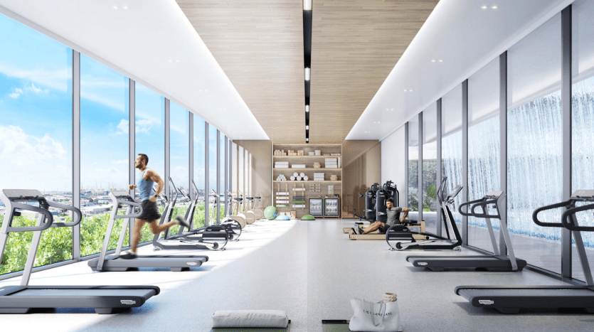 Une salle de sport moderne dans une villa à Dubaï avec des baies vitrées, des tapis roulants alignés, un homme qui court dessus et divers équipements d'exercice dispersés dans un espace soigné et lumineux.