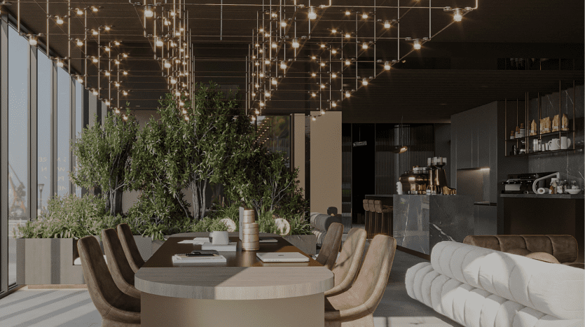 Modern office lounge with circular table, soft chairs, hanging lights and large indoor trees. Panoramic windows offer views of the city of Dubai.